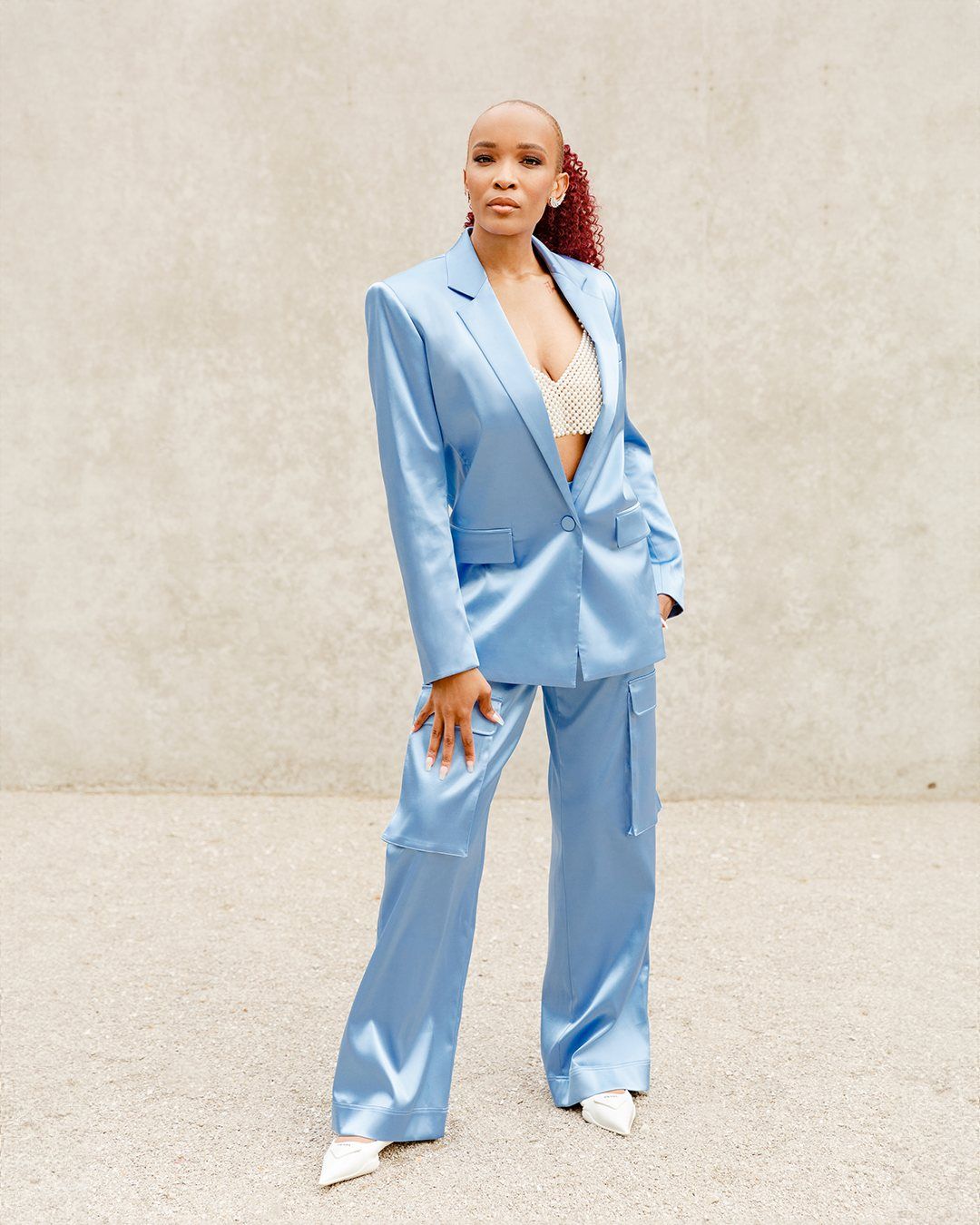 Florie Naomi in a satin blue suit against a concrete wall